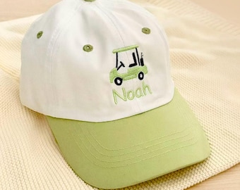 Op de afbeelding: Witte en groene baseballcap met een golfkarretje geborduurd in groen. De cap heeft de naam "Noah" in groen geborduurd. De klep en de knoop zijn groen.