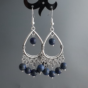 Peut inclure: Boucles d'oreilles pendantes en argent avec un design en forme de larme et des perles de pierres précieuses bleues.