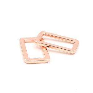 May include: Two rose gold metal rectangular rings, one on top of the other.