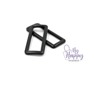 May include: Two black metal rectangular frame buckles. The buckles are stacked on top of each other.