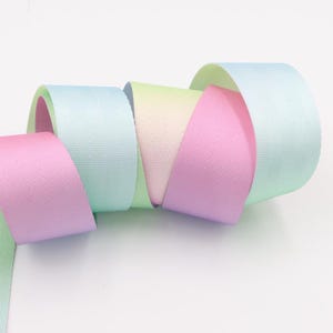 May include: A close-up of a collection of pastel colored ribbon spools. The ribbon is a satin material and is arranged in a spiral shape. The colors are light green, light blue, pink, and a light yellow.