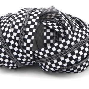 May include: A close-up of a black and white checkered zipper tape. The tape is made of a woven fabric with a silver zipper.