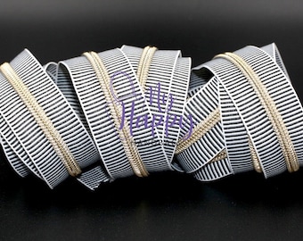 May include: A coiled zipper with a black and white striped pattern and a gold-coloured zipper track. The zipper is made of a woven material and is displayed against a black background. The text "Happy Handmade" is partially visible.