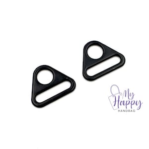 May include: Two black triangle-shaped metal D-rings with a small hole at the top and a larger opening in the middle.