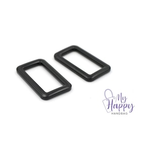 May include: Two black metal D-rings, each with a rectangular shape and a smooth finish.