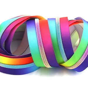 May include: A close-up of a collection of rainbow colored zippers with silver teeth. The zippers are arranged in a circle and are all different shades of rainbow.