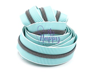May include: A close-up of a teal and white striped zipper with a silver metal zipper pull. The zipper is coiled up and ready to be used for a sewing project.