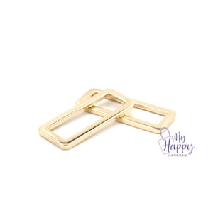 May include: Two gold-colored metal rectangular rings, likely for attaching to a handbag or purse.