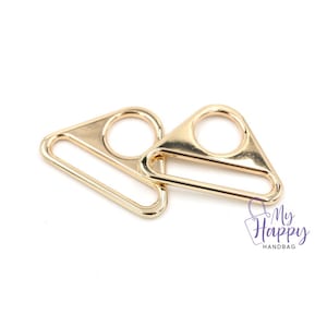 May include: Two gold-toned metal triangle-shaped D-rings with a smooth finish.