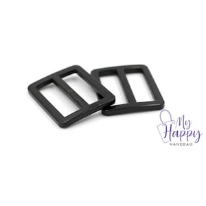 May include: Two black plastic slider buckles. The buckles are rectangular with two holes in the center.