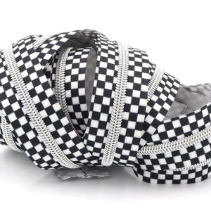 May include: A close-up of a black and white checkered zipper tape. The tape is coiled and twisted, showing the silver zipper teeth.