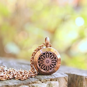 May include: A gold-toned necklace with a round pendant featuring a detailed floral design. The pendant is open on the back, suggesting it may be an aromatherapy diffuser.