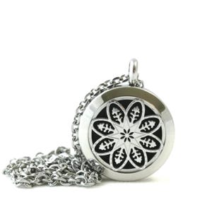 May include: A circular silver-toned metal pendant necklace featuring a cut-out floral pattern with eight symmetrical petals over a black background. The pendant is attached to a matching silver-toned link chain that rests in a coiled pile.