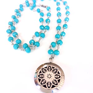 May include: A necklace featuring a chain of faceted bright turquoise beads linked with silver-toned wire. The pendant is a circular silver-toned locket with a cut-out geometric star pattern revealing a black background underneath the metal design.