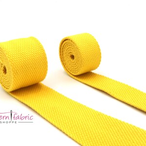 Può includere: Due rotoli di fettuccia di cotone giallo brillante, un tipo di tessuto piatto tessuto utilizzato per cinghie, cinture e altri progetti di artigianato.