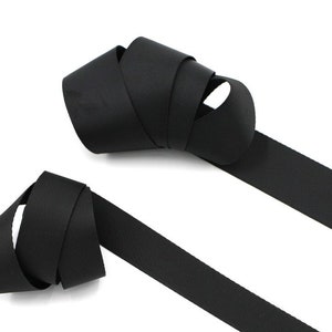 Puede incluir: Dos piezas de cinta negra, una está doblada y la otra está recta.