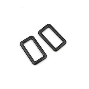 Puede incluir: Dos anillos rectangulares de metal negro, cada uno con un borde liso y redondeado.