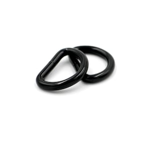 May include: Two black metal D-rings, also known as D rings or D-shackles, are shown on a white background. These rings are commonly used for attaching straps, chains, or other hardware.