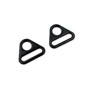 Pode incluir: Dois anéis de metal de forma triangular preta com um pequeno furo e uma abertura retangular maior. Esses anéis são frequentemente usados para prender correias ou outros acessórios.