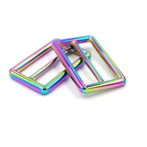 May include: Two iridescent rainbow-colored metal slider buckles. The buckles are rectangular with a rounded edge and have a smooth, shiny finish.