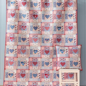 Könnte beinhalten: Ein Patchwork-Quilt und ein passendes quadratisches Kissen mit einem sich wiederholenden Gittermuster aus Herzen. Der Stoff zeigt verschiedene Blumen-, Vichy- und geometrische Drucke in Rot-, Blau- und Weißtönen mit roter Umrandung.