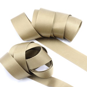 Peut inclure: Deux rouleaux de sangle beige, un type de tissu solide et tissé souvent utilisé pour les sangles et les ceintures.