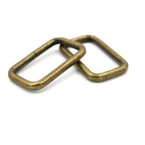 May include: Two antique gold-toned metal D-rings. The rings are rectangular in shape and have a smooth, slightly textured finish.