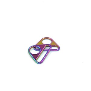 Pode incluir: Dois anéis em D de metal iridescente, um em cima do outro. Os anéis são um arco-íris de cores, incluindo roxo, azul, verde, amarelo e laranja.