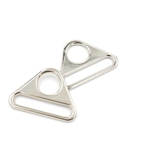 Pode incluir: Duas fivelas deslizantes de metal de forma triangular prateadas. As fivelas têm um furo redondo e uma ranhura longa.