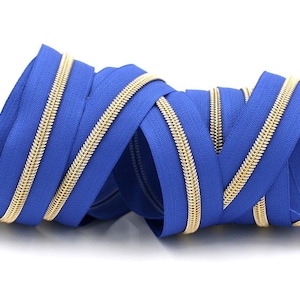 May include: A close-up of a blue zipper with gold teeth. The zipper is coiled and twisted, showing off the details of the metal teeth and the blue fabric.