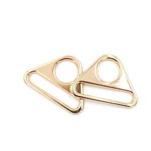 May include: Two gold-toned metal triangle-shaped slider buckles with a round opening and a rectangular opening.