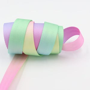 Puede incluir: Un rollo de cinta de colores pastel con efecto degradado. La cinta es rosa, amarilla, verde y azul.