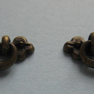 Könnte beinhalten: Zwei antike Messing-Schubladengriffe mit dekorativem Design. Jeder Griff hat einen Schleifen-Griff und eine dekorative Rückplatte.