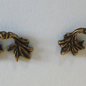 Puede incluir: Dos tiradores de cajón de metal en forma de hoja, de color dorado. Cada tirador tiene un diseño curvo abierto con un bucle central.