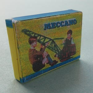 May include: A vintage Meccano box with a yellow side and a blue top. The front features a colorful illustration of two children operating a green crane. The word "MECCANO" is printed in blue across the top of the box.