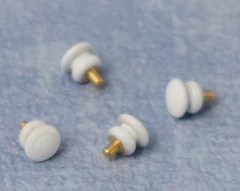 May include: Four white ceramic knobs with gold metal stems. The knobs are round and have a slightly raised center. They are arranged in a semi-circle on a light blue surface.