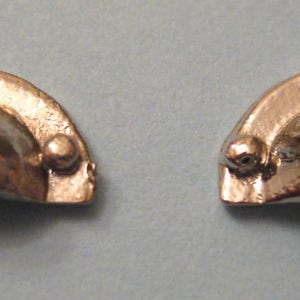 以下が含まれることがあります： 2つの銀色の金属製の部品。丸みを帯びた湾曲した形をしていて、両側に3つの小さな丸い突起があります。部品はデザインが似ており、装飾的なようです。