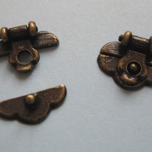 May include: Three antique gold-toned metal clasps with decorative details. The clasps are shaped like a flower with a small round knob in the centre.