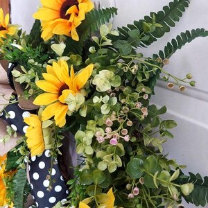 Angled view of handmade sunflower wreath with greenery and black‑and‑white bow.