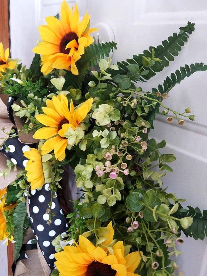 Angled view of handmade sunflower wreath with greenery and black‑and‑white bow.