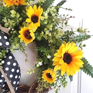 Close‑up of bright faux sunflowers and realistic greenery on summer wreath.