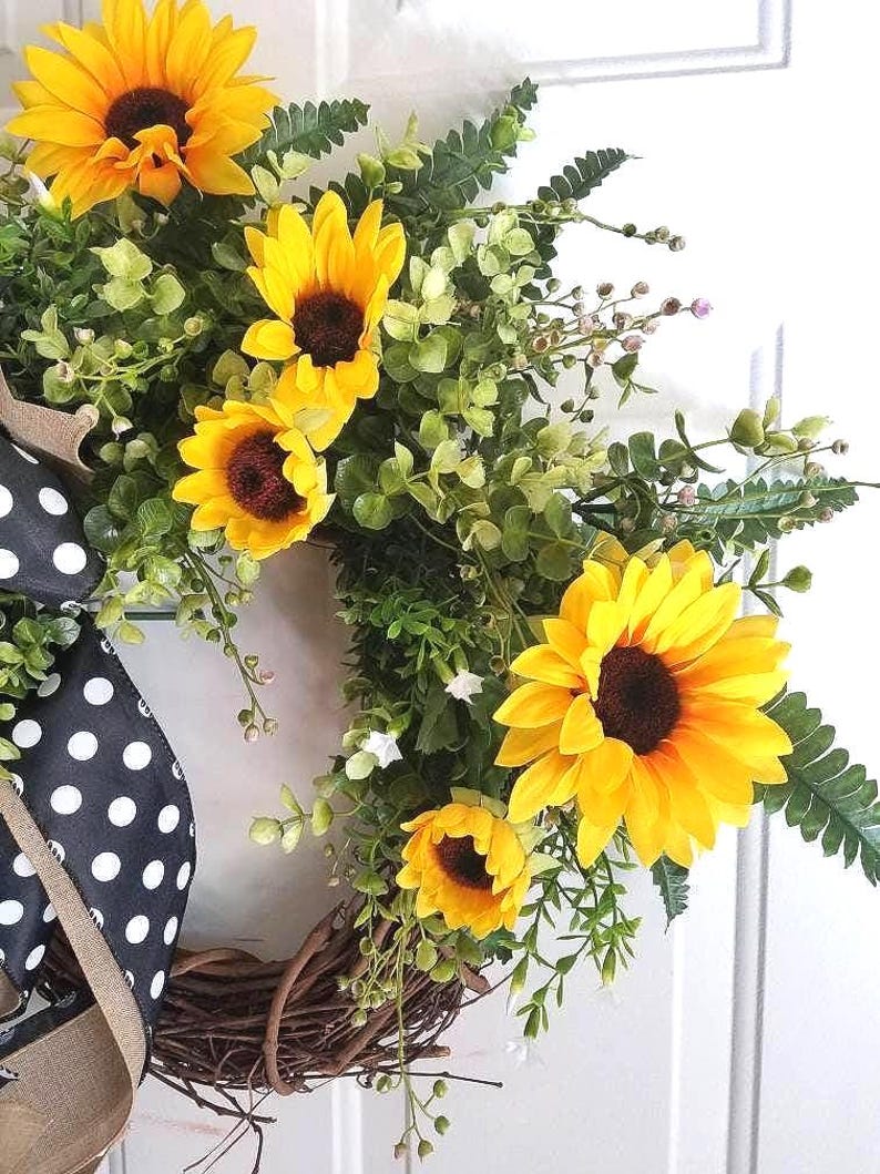 Close‑up of bright faux sunflowers and realistic greenery on summer wreath.
