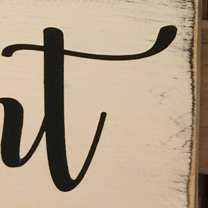 May include: A close-up of a white wooden sign with the word "sweet" in black cursive lettering. The sign has a distressed, vintage look with slightly worn edges, adding to its rustic charm.