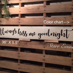 May include: A rectangular, off-white wooden sign with the phrase "Always kiss me goodnight" in black script. The sign measures 91.4 cm long and 14 cm wide. The background is a wooden pallet.