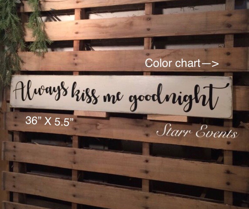 May include: A rectangular, off-white wooden sign with the phrase "Always kiss me goodnight" in black script. The sign measures 91.4 cm long and 14 cm wide. The background is a wooden pallet.
