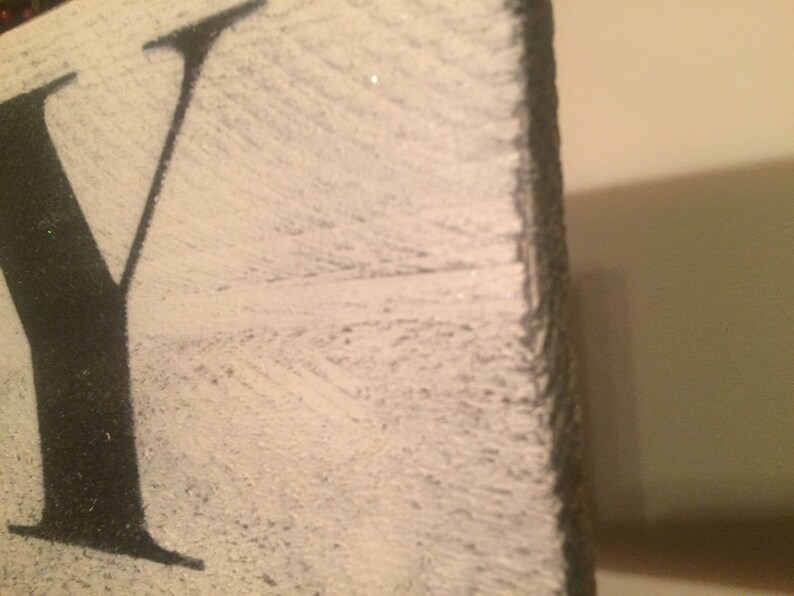 May include: Close-up of a distressed wooden sign with the letter "Y" in black against a white background. The wood has a textured, weathered appearance, with visible grain and a slightly rough edge. The sign is likely for home decor.