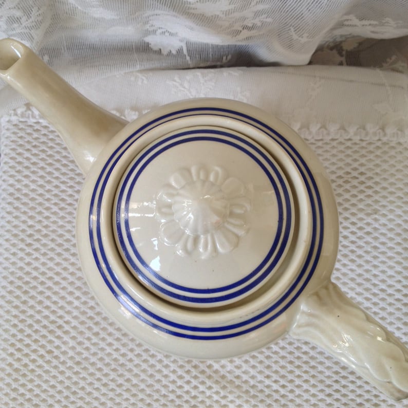 Pu&ograve; includere: Teiera in ceramica bianca con un designo floreale blu e bianco. La teiera ha un corpo rotondo e un beccuccio. Il coperchio ha un designo floreale in rilievo.
