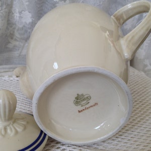 Pu&ograve; includere: Una teiera in ceramica bianca con un coperchio e un manico. La teiera ha un logo verde e oro sul fondo che recita "Bavaria" e "handgemalt".