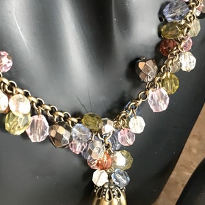 Puede incluir: Un collar de cadena dorada con una variedad de cuentas de vidrio de colores y un colgante decorativo de oro. Las cuentas son en tonos de rosa, azul, verde y marr&oacute;n.