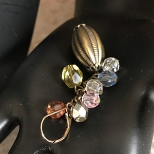 Puede incluir: Un pendiente de plata con un dije en forma de l&aacute;grima y un racimo de cuentas de vidrio de colores en tonos rosa, azul, amarillo y transparente.